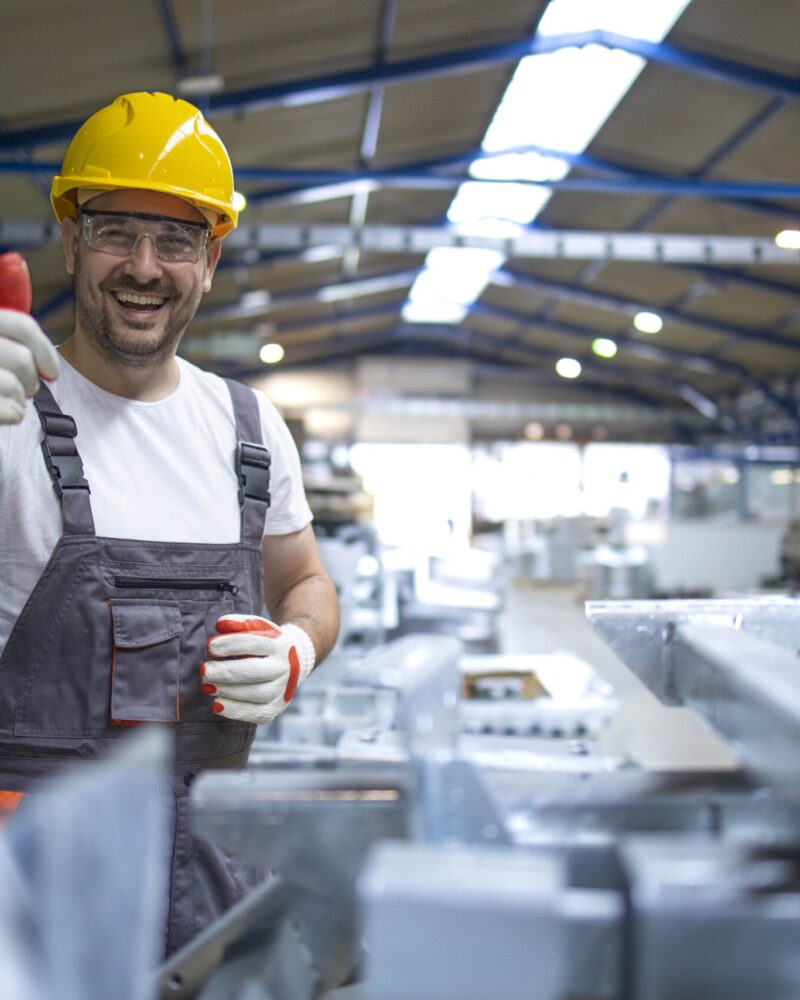 portrait-ouvrier-usine-dans-equipement-protection-holding-thumbs-up-in-production-hall-min